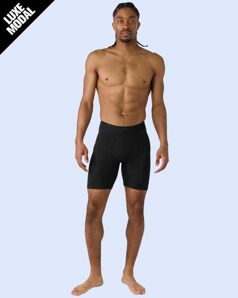 Man wearing black modal shorts standing against light blue background.