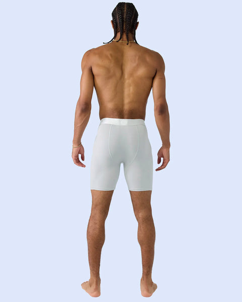 Man wearing white knee-length boxer briefs, shown from behind against light blue background.