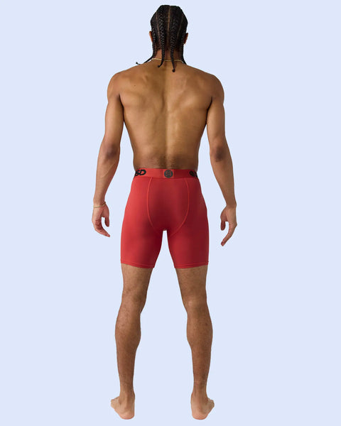 Man wearing red boxer briefs with metallic sheen and branded waistband, shown from back view.