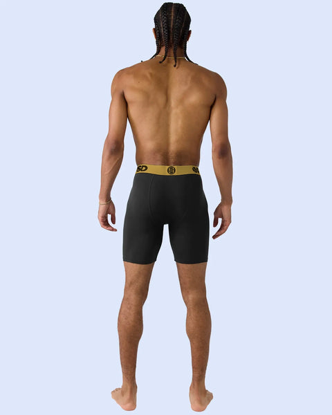Man wearing black boxer briefs with gold waistband, shown from behind against light blue background.