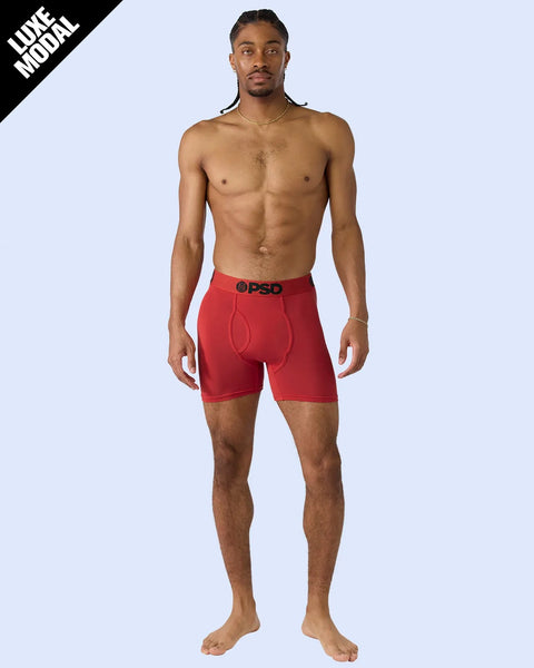 Man wearing red modal boxer briefs with black waistband against light blue background.