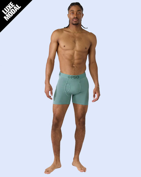 Man wearing sage green modal boxer briefs with branded waistband against light blue background.