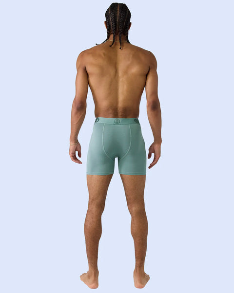 Man wearing sage green boxer briefs with square logo detail on waistband, shown from back.