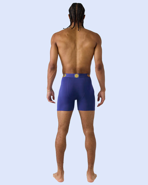 Man wearing royal blue boxer briefs with gold button detail, shown from back view.
