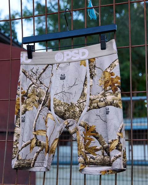 PSD Realtree Edge grey camouflage boxer shorts with tree and leaf print hanging on blue hanger.