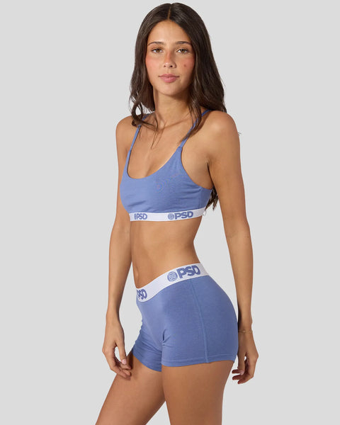 Woman wearing blue denim modal sports bra and shorts with white waistband detail.