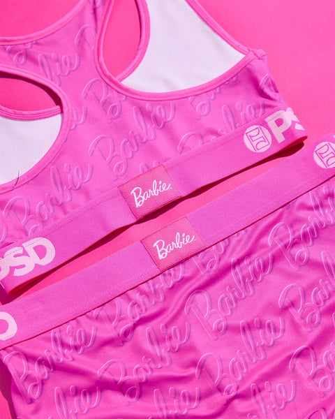 Pink sports bra with repeated Barbie branding and logos throughout fabric.