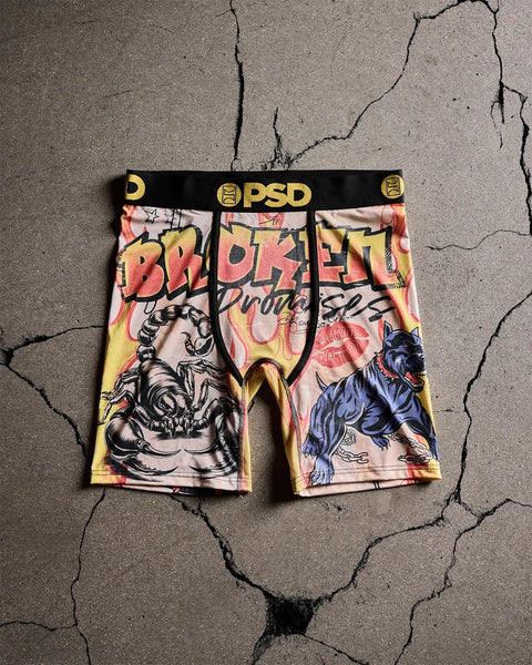 PSD boxer briefs with scorpion and animal graphics in yellow, pink, and black on cracked concrete background.
