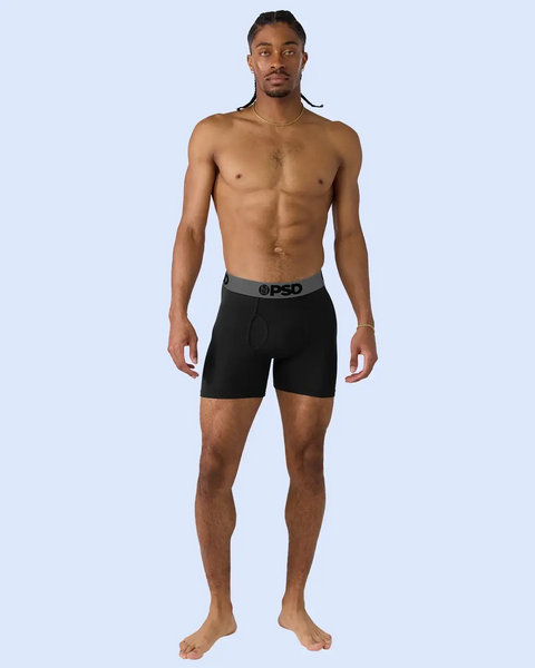 Man wearing black boxer shorts with grey waistband printed with PSD logo.