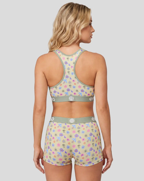 Woman wearing colorful mushroom-print sports bra and matching shorts with sage green trim and silver buckle details.