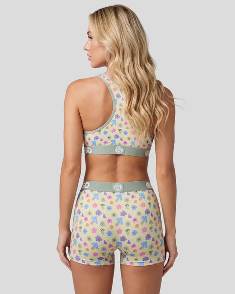 Woman wearing matching sports bra and shorts with multicolored mushroom print and sage green trim, shown from back.