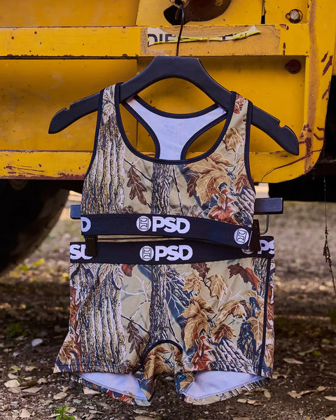 PSD brand two-piece tank and shorts set with Realtree Xtra camouflage pattern in grey tones and navy accents.