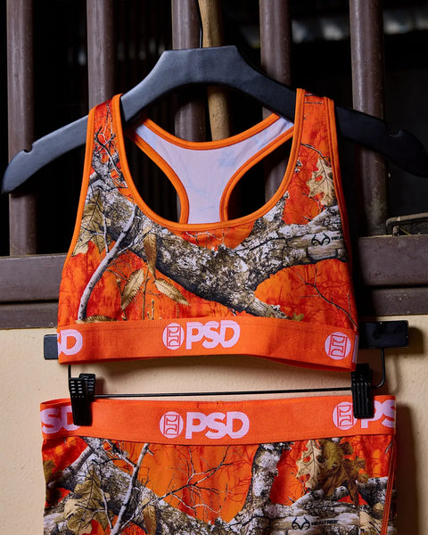 Sports bra with orange Realtree camouflage pattern, light purple lining, and PSD branding on elastic band.