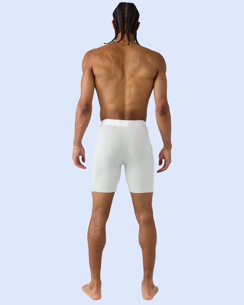 Man wearing white knee-length shorts with elastic waistband, shown from back view against light blue background.
