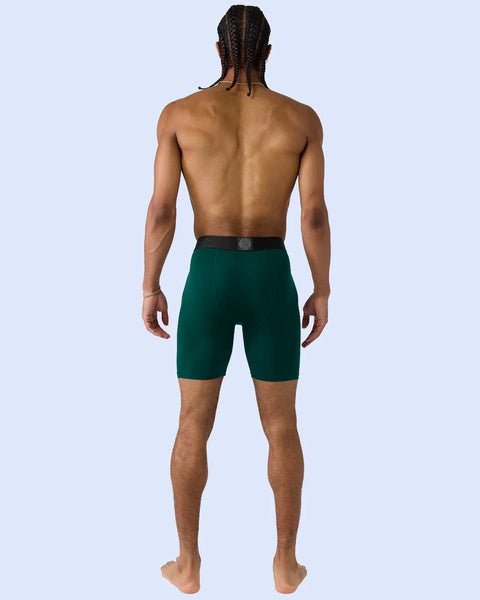 Man wearing deep green shorts with dark waistband, shown from behind against light blue background.