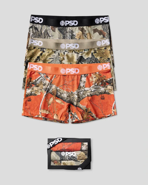 Three PSD boxer briefs in Realtree camouflage patterns with black, tan, and orange bands and packaging box below.