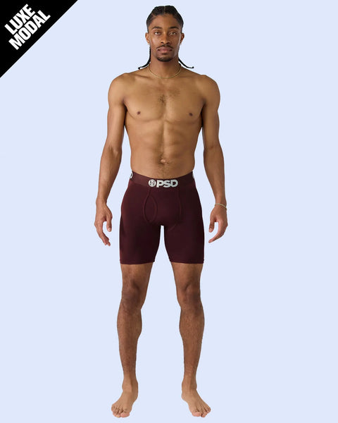 Man wearing burgundy modal shorts with PSD waistband against light blue background.