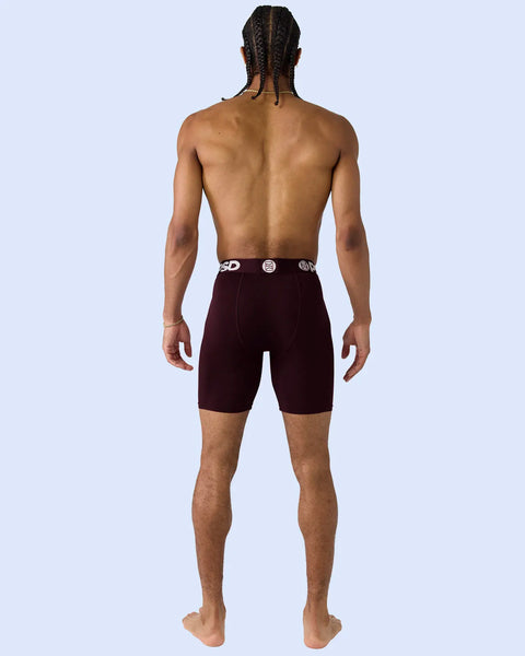 Man wearing burgundy boxer briefs with elastic waistband, shown from behind against light blue background.