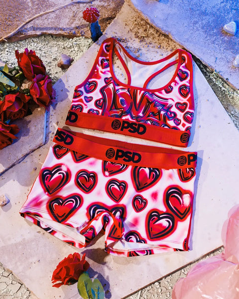 Red sports bra and shorts set with heart print and PSD branding displayed on concrete surface.